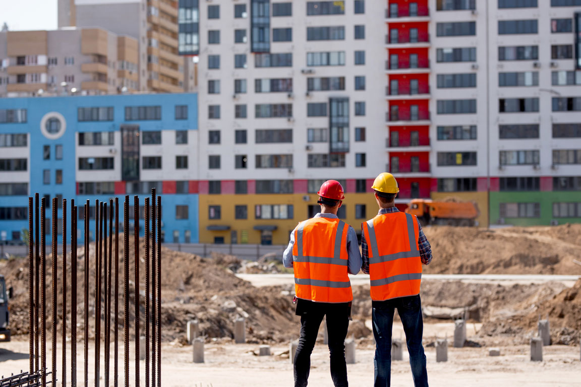 two-men-dressed-in-orange-work-vests-and-helmets two construction workers evaluating site